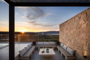 Un espace extérieur moderne, aménagé avec des sièges, un mur en pierre et offrant une vue sur le coucher de soleil au-dessus d’un paysage urbain.