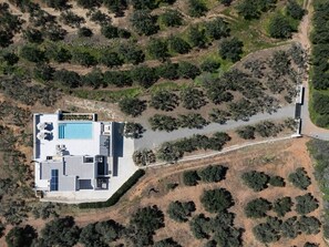 Luchtbeeld van een modern huis met zwembad, gelegen in een glooiend landschap met schaarse begroeiing.