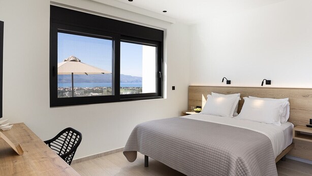 A modern bedroom with a large bed, a desk, and a window with a view of the sea. - Villa Kafkales | Heated Pool (Chania)