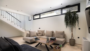 En moderne stue med trappe, sofaarrangement, sofabord og en potteplante.