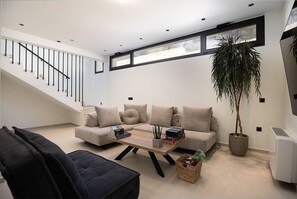 Een moderne woonkamer met een trap, een zithoek, een salontafel en een potplant.