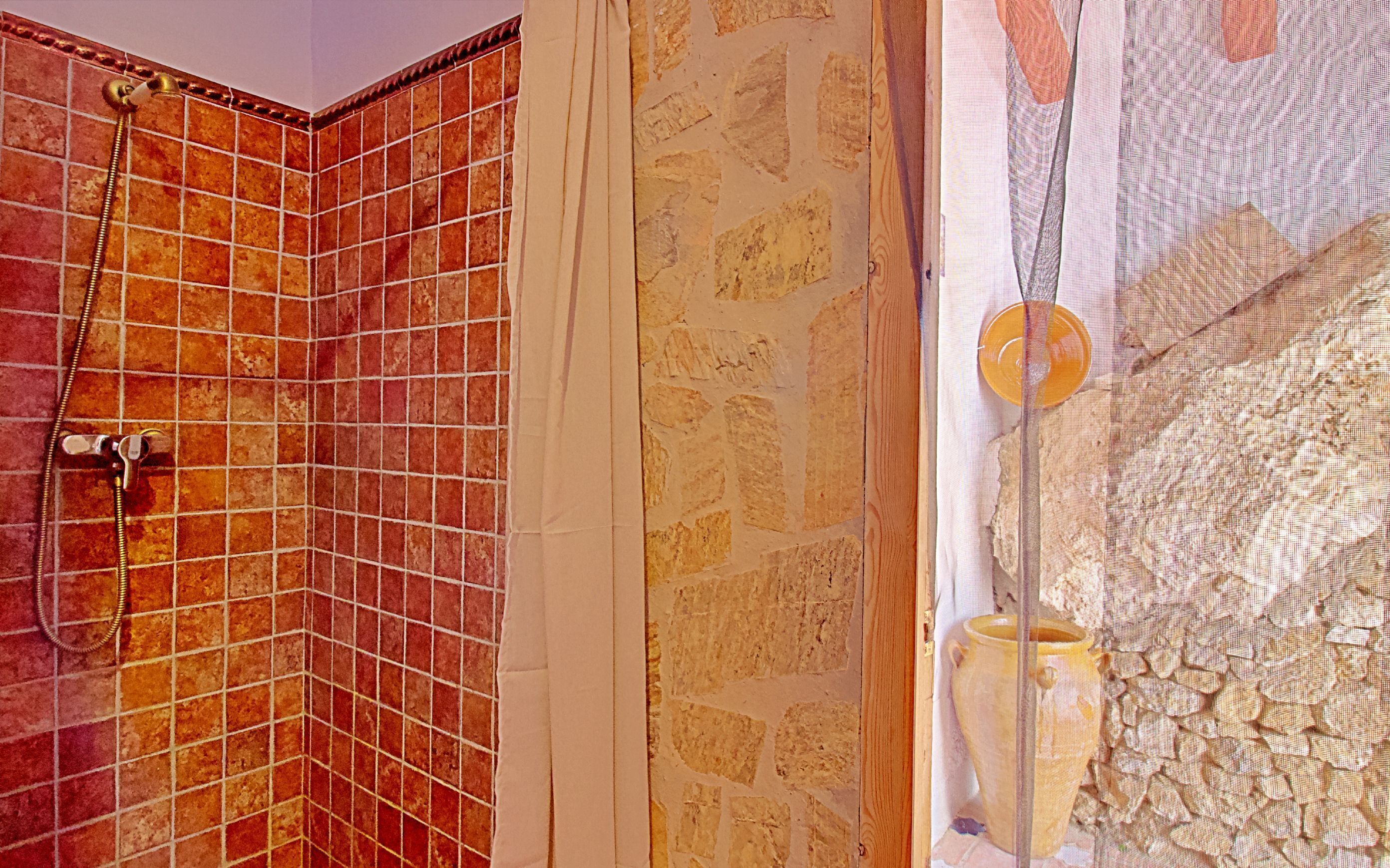 Ein Badezimmer mit gefliestem Duschbereich, einer Steinwand und einer dekorativen Glasplatte mit einer Vase.