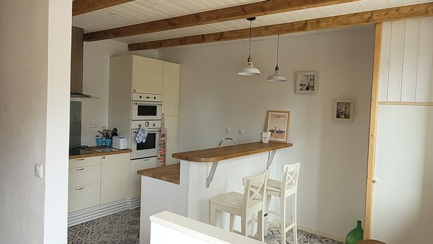 Una cocina con vigas de madera, armarios blancos y suelo de baldosas.
