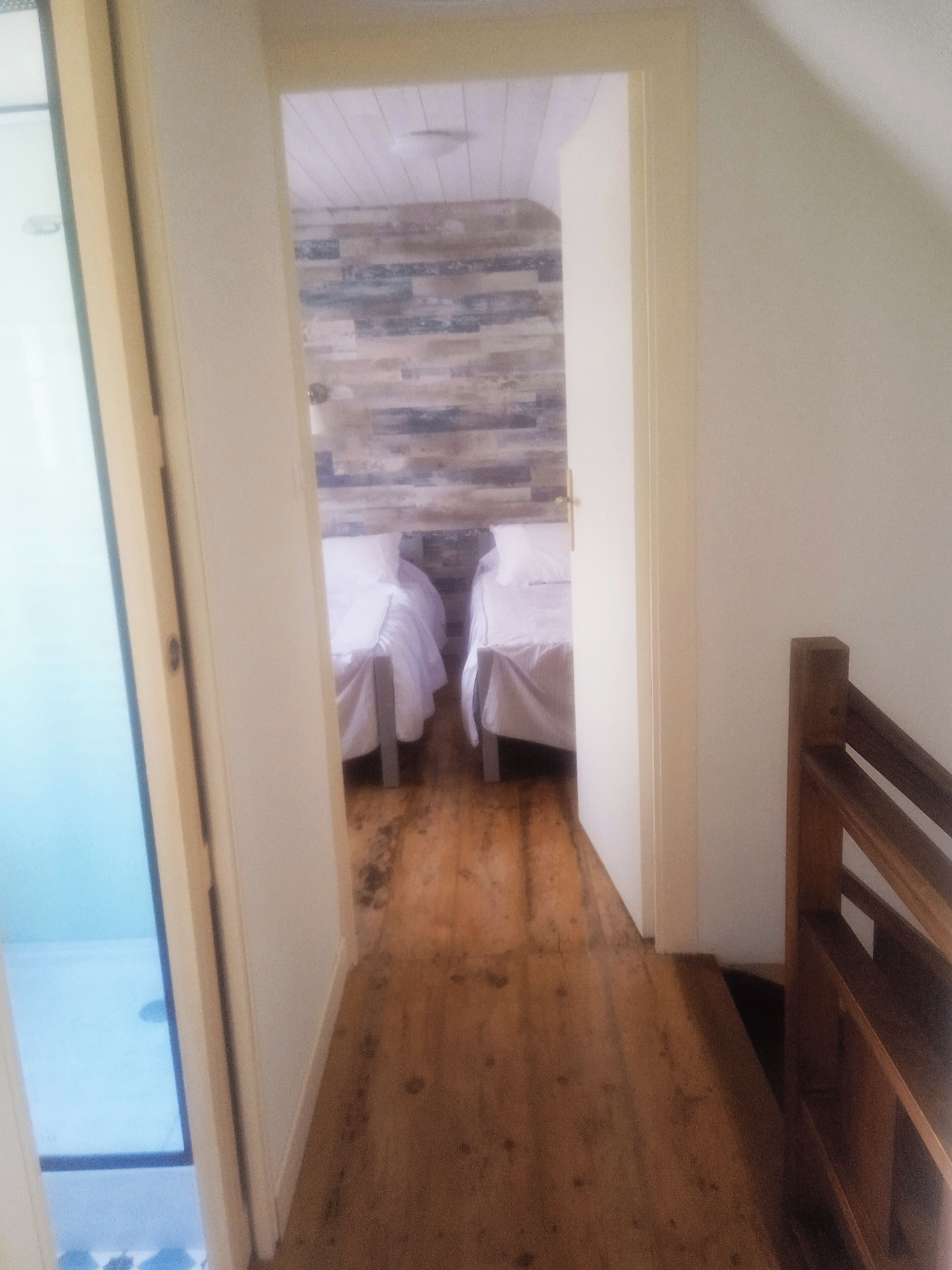 A narrow hallway leading to a room with two beds, wooden flooring, and a sloped ceiling.