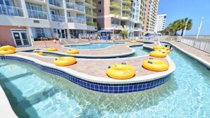 A swimming pool with yellow floating rings, surrounded by a tiled deck and a multi-story building with balconies. - Oceanfront King Bed 2BR 2BA Condo with WD Kitchen (North Myrtle Beach)