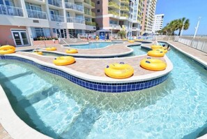 A swimming pool with yellow floating rings, surrounded by a tiled deck and a multi-story building with balconies.