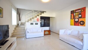 A modern living room with a staircase, white sofas, a flat-screen TV, and a colorful abstract painting. - 3 bedroom cozy home in Lavinio (Lavinio)