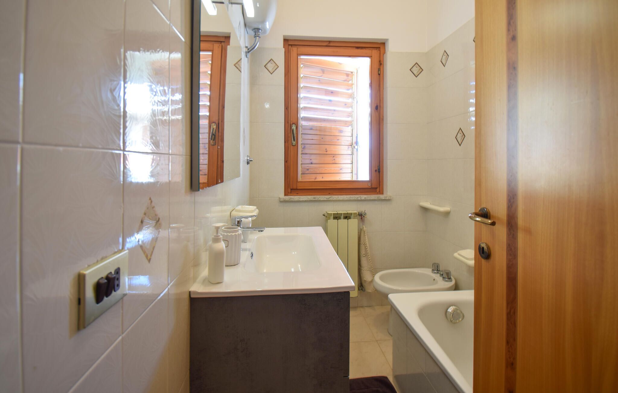 Een badkamer met een wastafel, spiegel en raam.