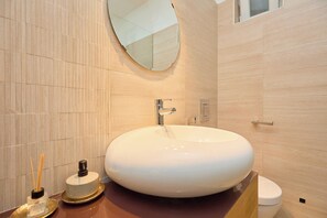 A modern bathroom with a round white sink, a mirror above it, and a toilet to the right. - Cityview Apartment (Dubrovnik)