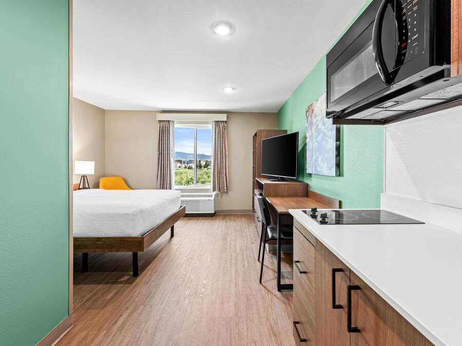 A compact hotel room with a bed, a desk, a microwave, and a TV.