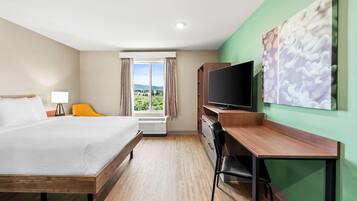 A hotel room with a bed, desk, chair, TV, and a window with curtains.