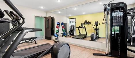 A gym with treadmills, an elliptical, weight machines, and a mirrored wall.