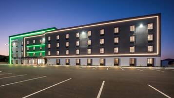 A modern hotel with a long facade, multiple floors, and a parking lot in front.