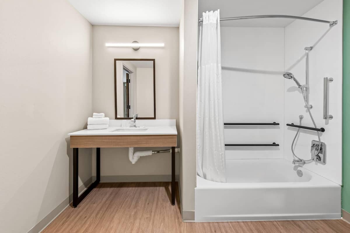 A modern bathroom with a wooden vanity, a white sink, a mirror, a shower with a curved glass door, and a white bathtub.