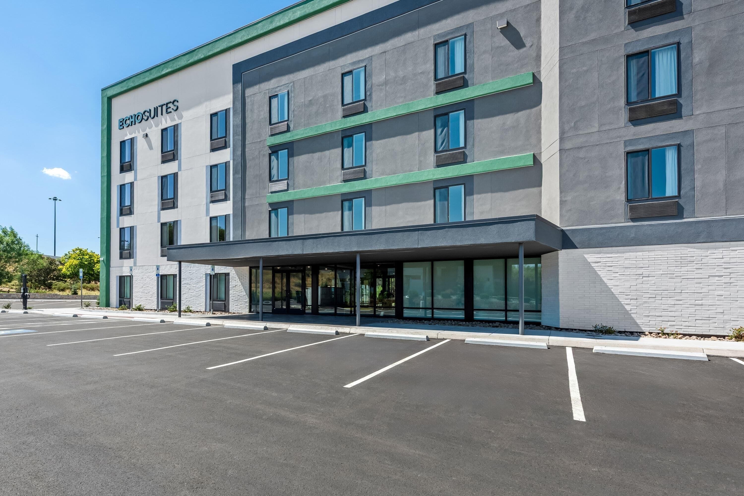 A modern hotel with a flat facade, multiple windows, and a parking lot in front.