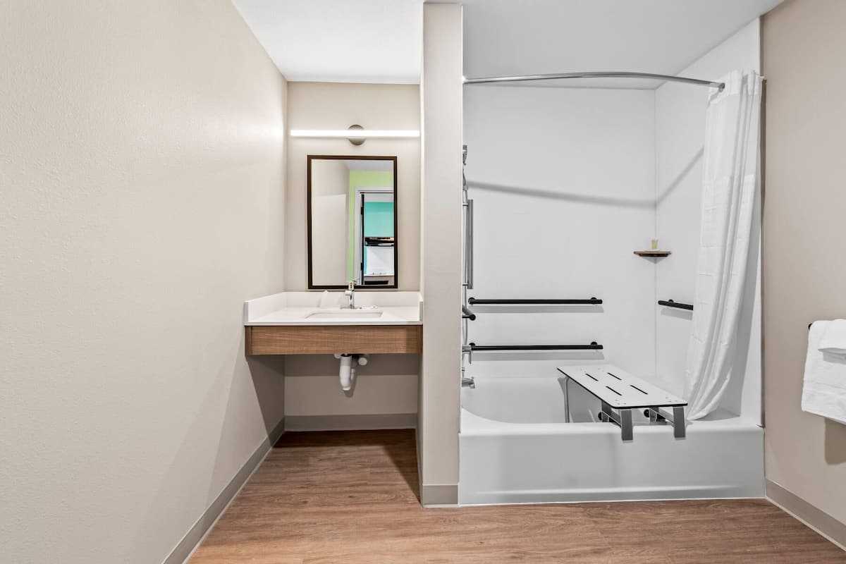 A modern bathroom with a wooden floor, a white sink, a mirror, and a shower area with a curtain.