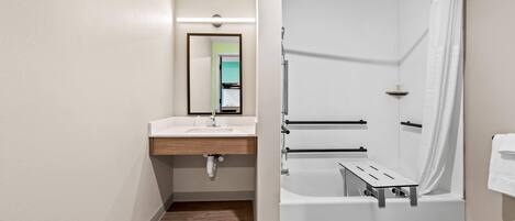 A modern bathroom with a wooden floor, a white sink, a mirror, and a shower area with a curtain.