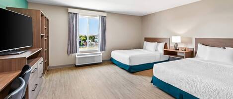 Habitación de hotel con dos camas, un escritorio con televisor, una ventana con cortinas y vistas al exterior.