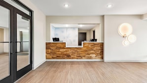 A reception area with a wooden reception desk, a large mirror, and a wall-mounted light fixture. - Echo Suites Extended Stay Reno (Reno)