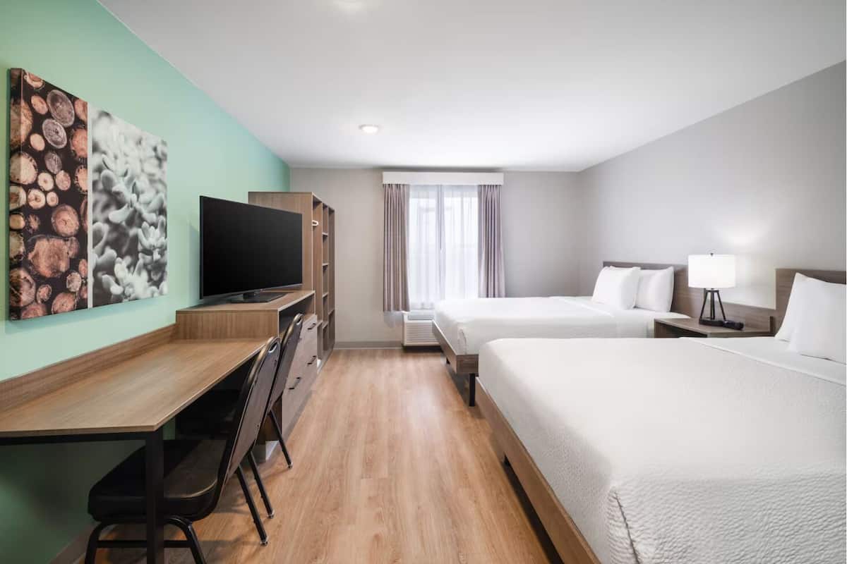 A hotel room with a desk, two beds, a TV, and artwork on the wall.