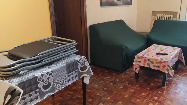 A room with a wooden parquet floor, a green sofa, a small table with a pineapple-patterned tablecloth, and a table with a geometric-patterned tablecloth. - Marvelous 2-bedroom apartment with WiFi in Móstoles (Móstoles)