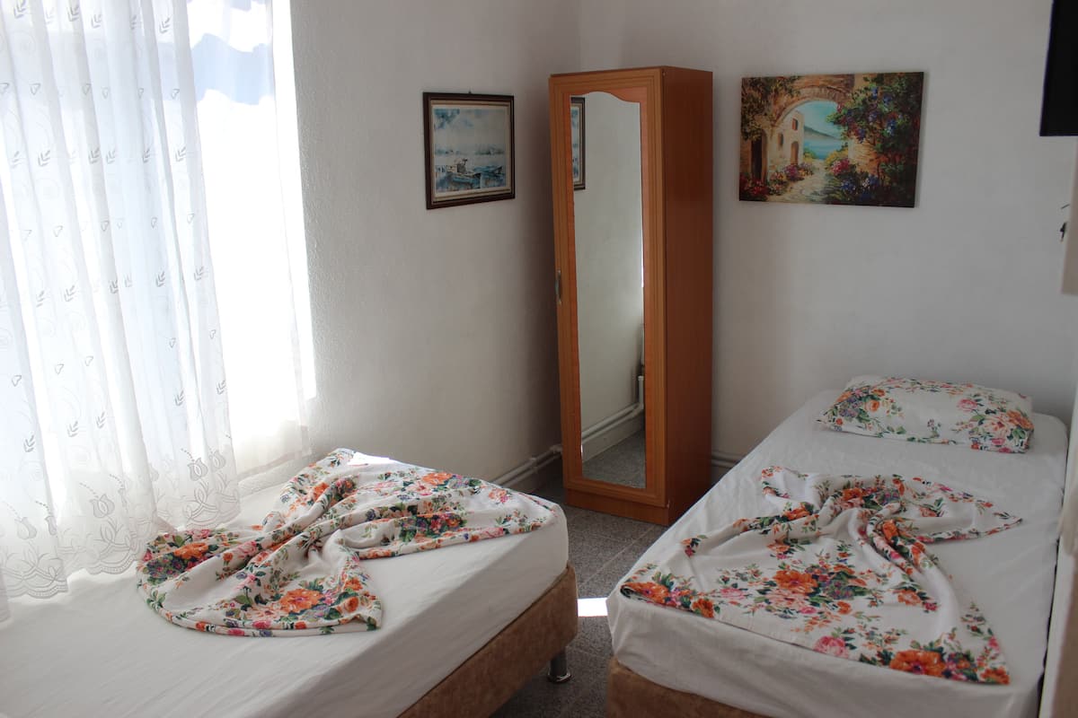 A bedroom with two beds, a wooden wardrobe, a mirror, and two framed pictures on the wall.