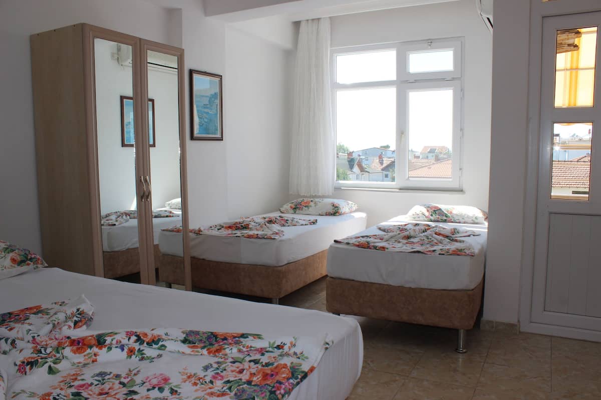 A bedroom with two single beds, a wardrobe, and a window with a view of buildings.
