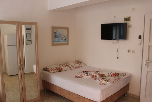 A bedroom with a bed, a television mounted on the wall, a painting on the wall, and a door leading to another room.