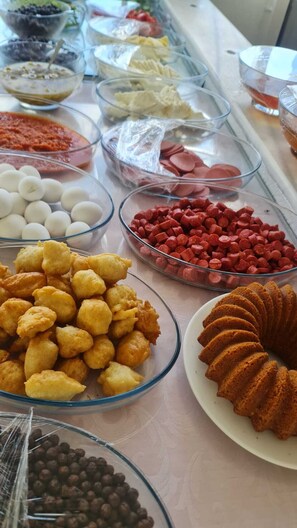 A buffet table with various food items including white and red candies, yellow fritters, and a bundt cake. - Aydın Motel (Marmara)