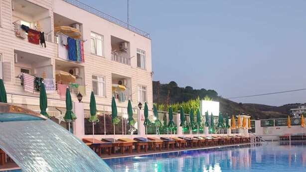 A swimming pool with a water slide, lounge chairs, umbrellas, and a building with balconies. - Aydın Motel (Marmara)