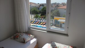 A bedroom with two beds, floral bedding, a window with a view of a pool and buildings. - Aydın Motel (Marmara)