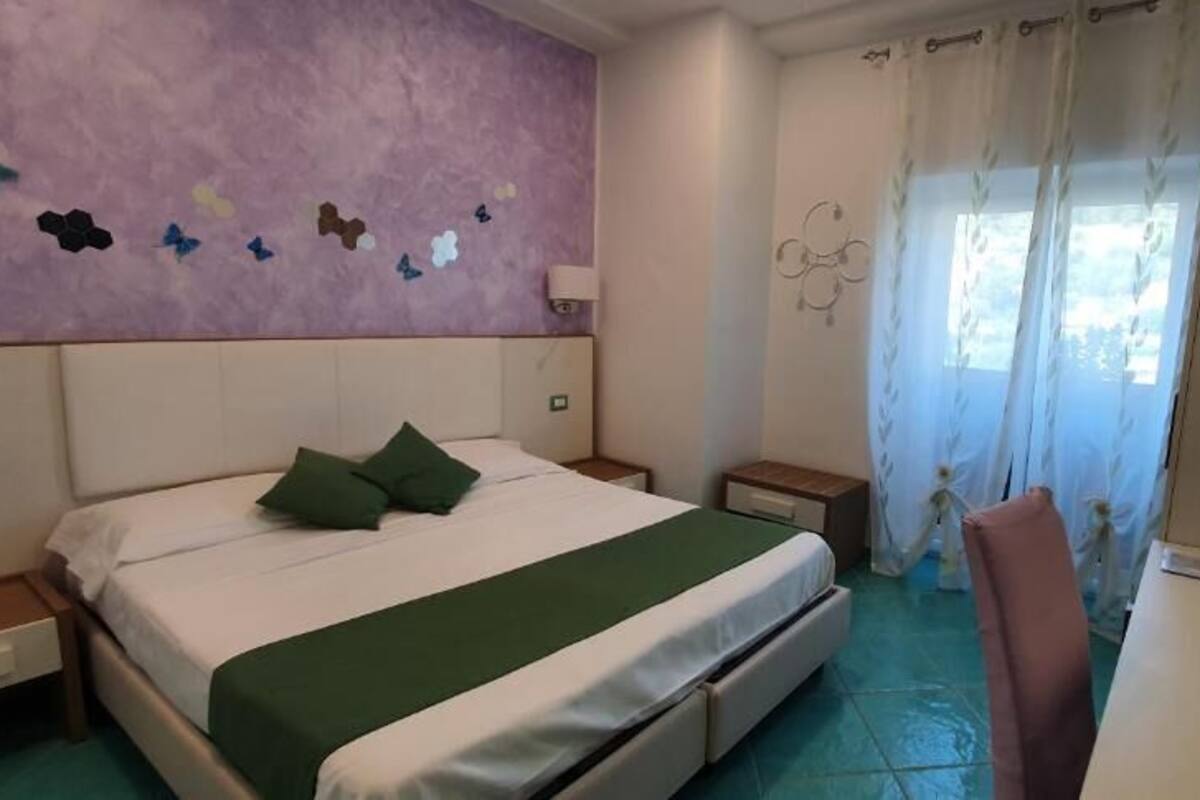 A bedroom with a bed, green pillows, a nightstand, a desk, and a chair.