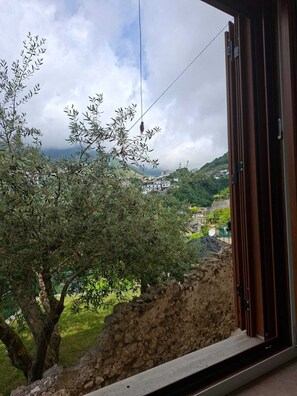 A view from a balcony with a stone wall, a tree, and a distant town. - Le perle d'italia (Ravello)