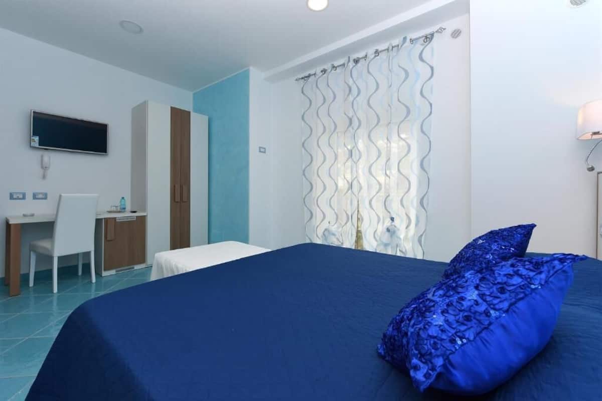 A hotel room with a bed, a desk, a chair, and a television.