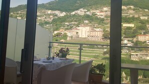 A terrace with a table and chairs, overlooking a hillside with buildings. - Le perle d'italia (Ravello)