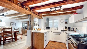Una cucina rustica con travi in legno a vista, pavimento in pietra e mobili bianchi, e un piano cottura a gas.