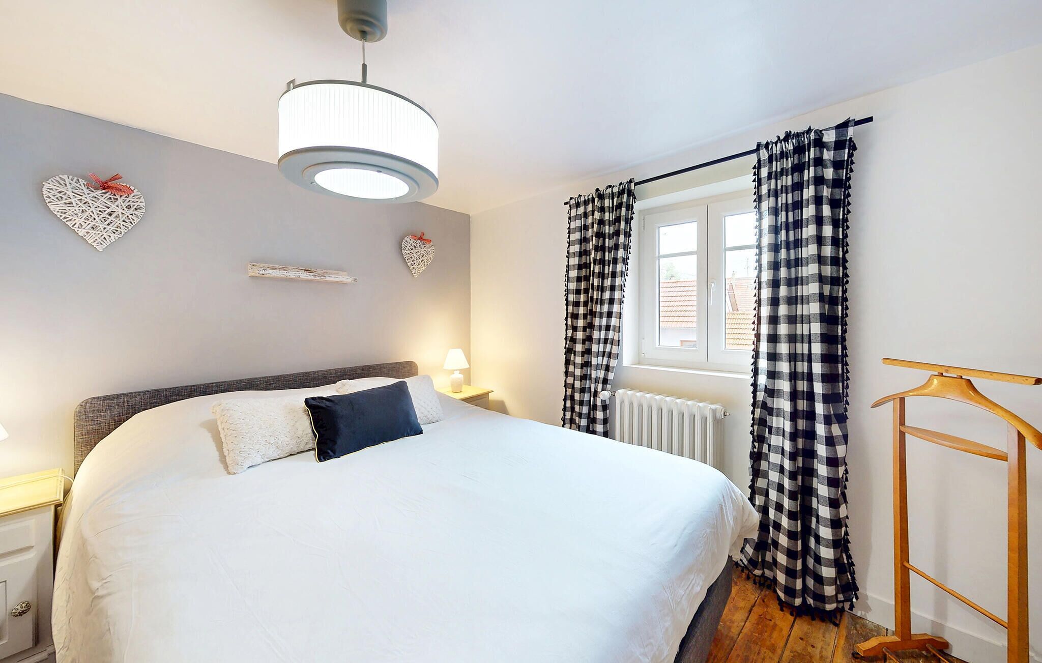 A bedroom with a bed, a hanging light fixture, a window with curtains, and decorative wall art.