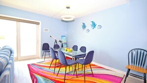 A dining area with a glass table, blue chairs, a colorful rug, and a ceiling light.
