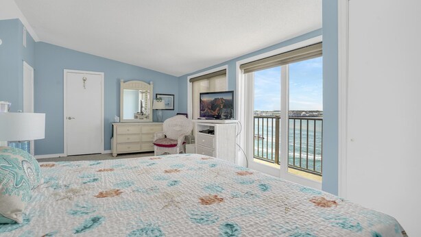 A bedroom with a bed, dresser, vanity, and a large window with a view of the ocean.