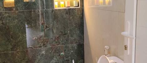 A bathroom with a marble wall, a white toilet, and wall-mounted lighting fixtures.