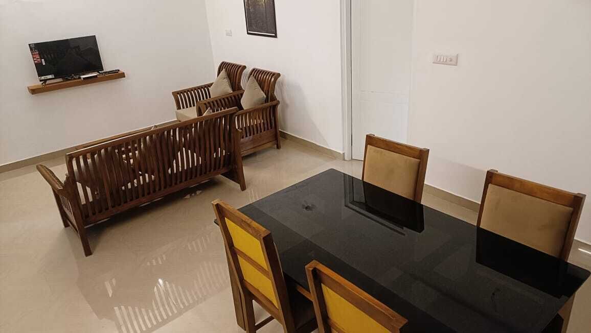 A dining area with a black table and wooden chairs, a sofa set, and a mounted TV.