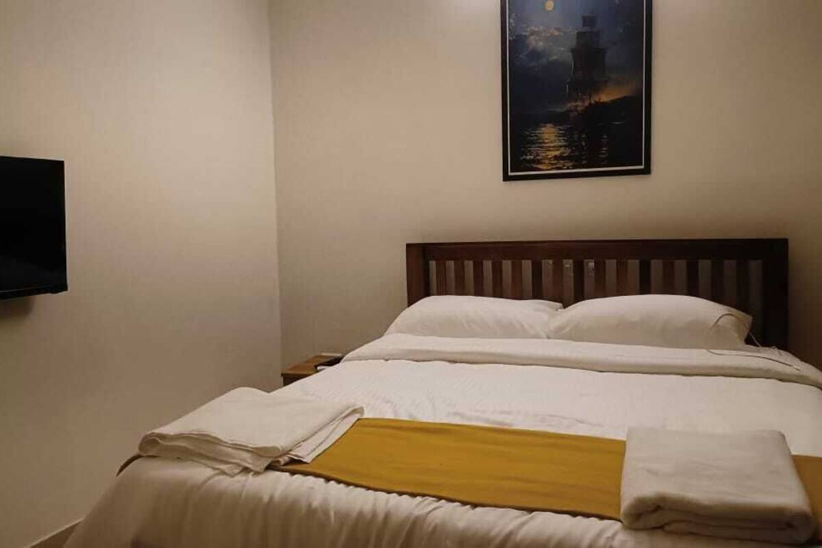 Hotellihuone, jossa on sänky, seinälle asennettu taulutelevisio ja sängyn yläpuolella oleva taulu.