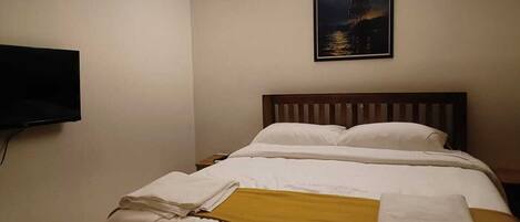 Habitación de hotel con cama, televisor de pantalla plana montado en la pared y un cuadro sobre la cama.