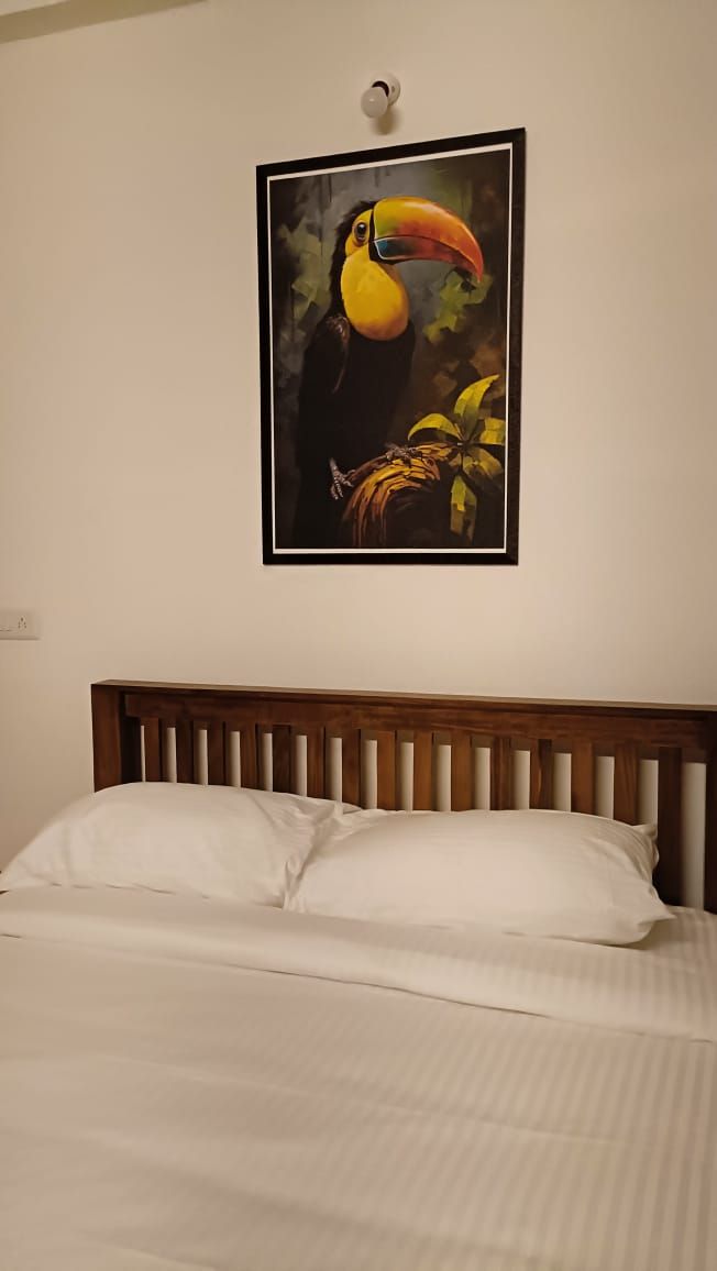 Ein Bett mit weißen Bettwäsche und einem Holzkopfteil, über dem Bett hängt ein gerahmtes Gemälde eines Tukan.