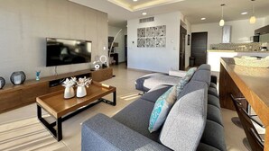 A modern living room with a large flat-screen TV, a wooden coffee table, and a grey sectional sofa.