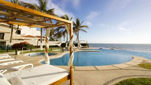A pool area with lounge chairs and a wooden pergola, overlooking the ocean.