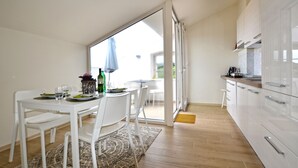 A modern kitchen with white cabinets, a dining area with white chairs, and a large sliding glass door leading to an outdoor area. - Tranquil Getaway With Shared Pool in Bale (Bale)
