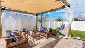 A covered patio area with wooden furniture, including a sofa and chairs, and a small table.