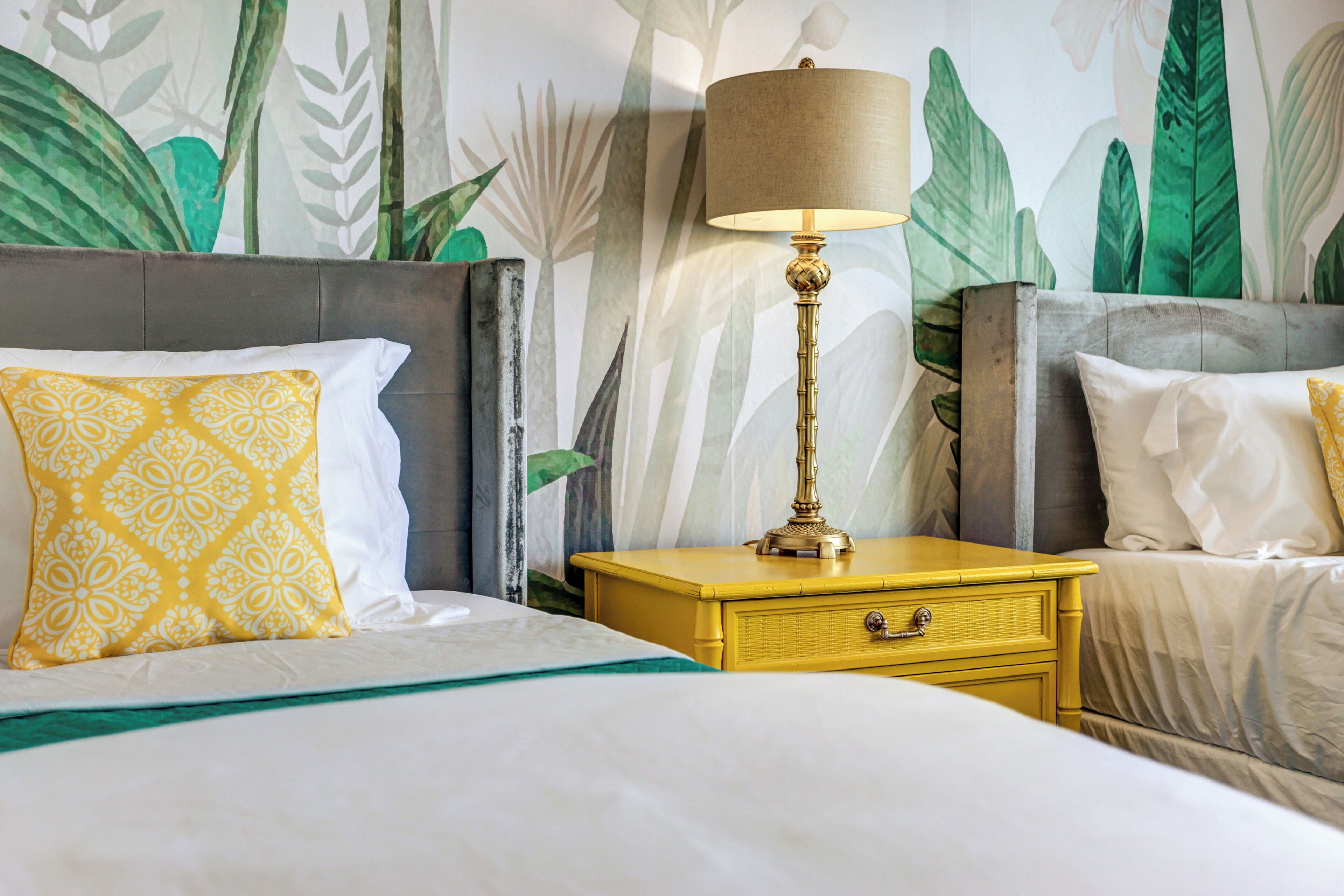 Une chambre d’hôtel avec un lit, une table de chevet avec une lampe et un mur orné d’un motif de feuilles tropicales.