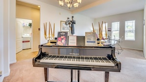 Un piano à queue dans une pièce spacieuse, agrémentée d’un lustre, d’une carte encadrée et d’une statue.